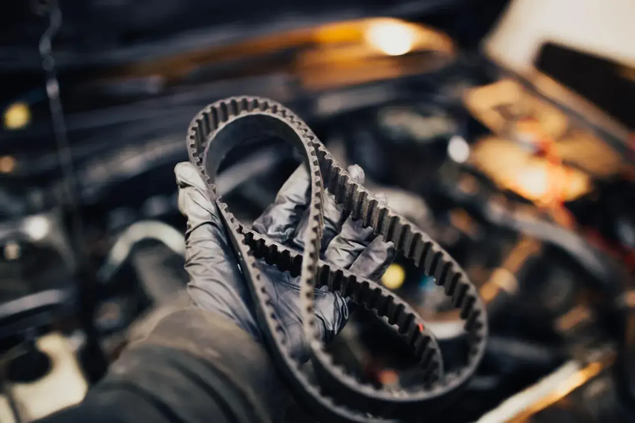 Rękawiczka mechanika trzyma pasek rozrządu. Sprawdź, jak sprawdzić czy rozrząd jest do wymiany, zanim dojdzie do awarii.