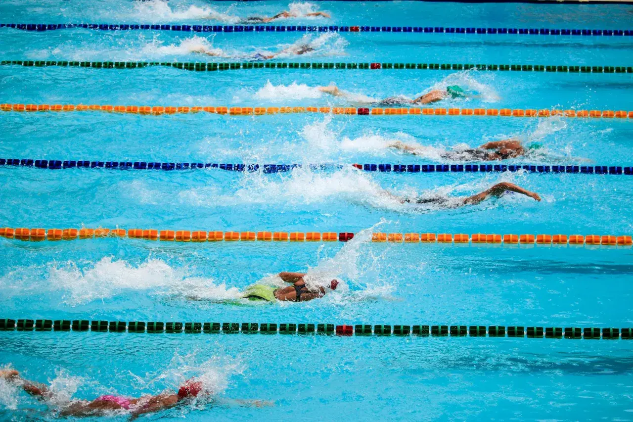 Zawodnicy w trakcie wyścigu pływackiego. Woda rozpryskuje się wokół nich, gdy wykonują ruchy. To dynamiczne sporty wodne po angielsku.