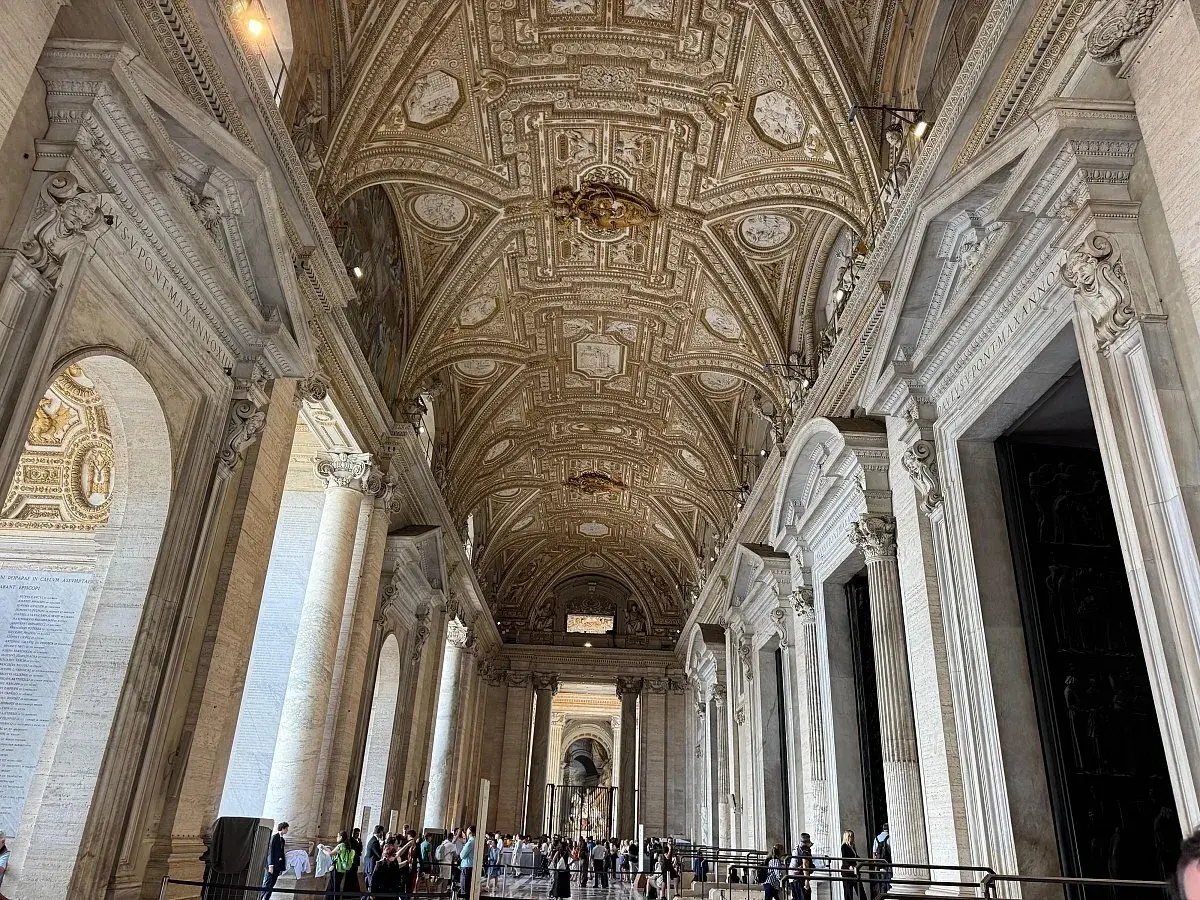 Interno della chiesa di San Pietro a Roma, con soffitto a cassettoni dorato e colonne imponenti.