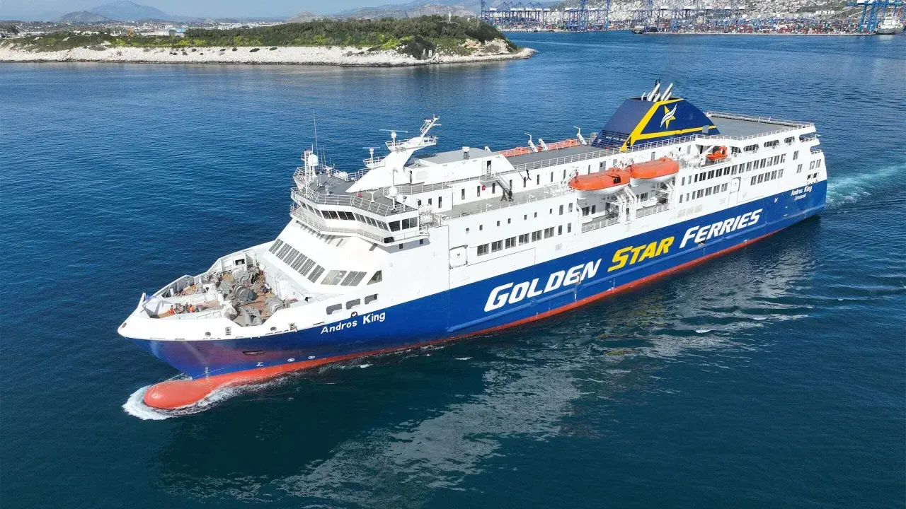 Prom "Andros King" Golden Star Ferries płynie po morzu. W tle widać port i góry.