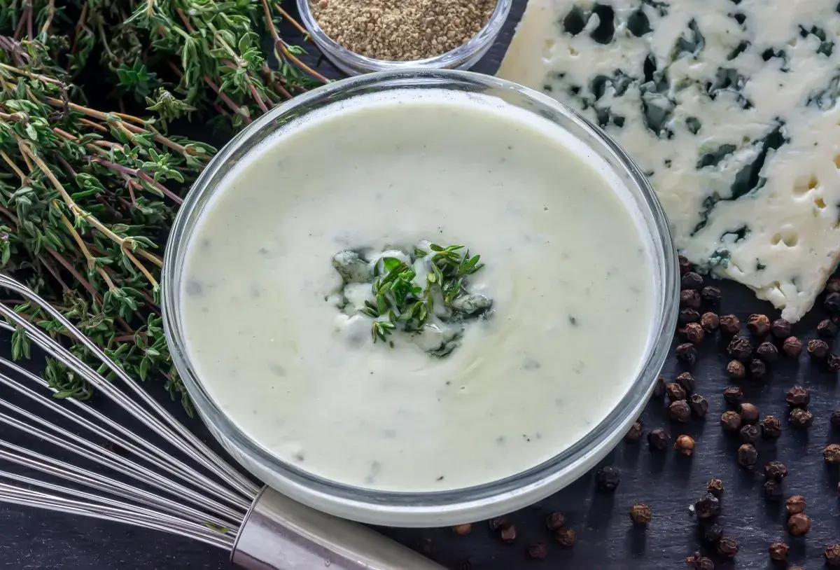 Crema suave con trozos de queso azul y tomillo fresco, lista para convertirse en una deliciosa salsa roquefort.