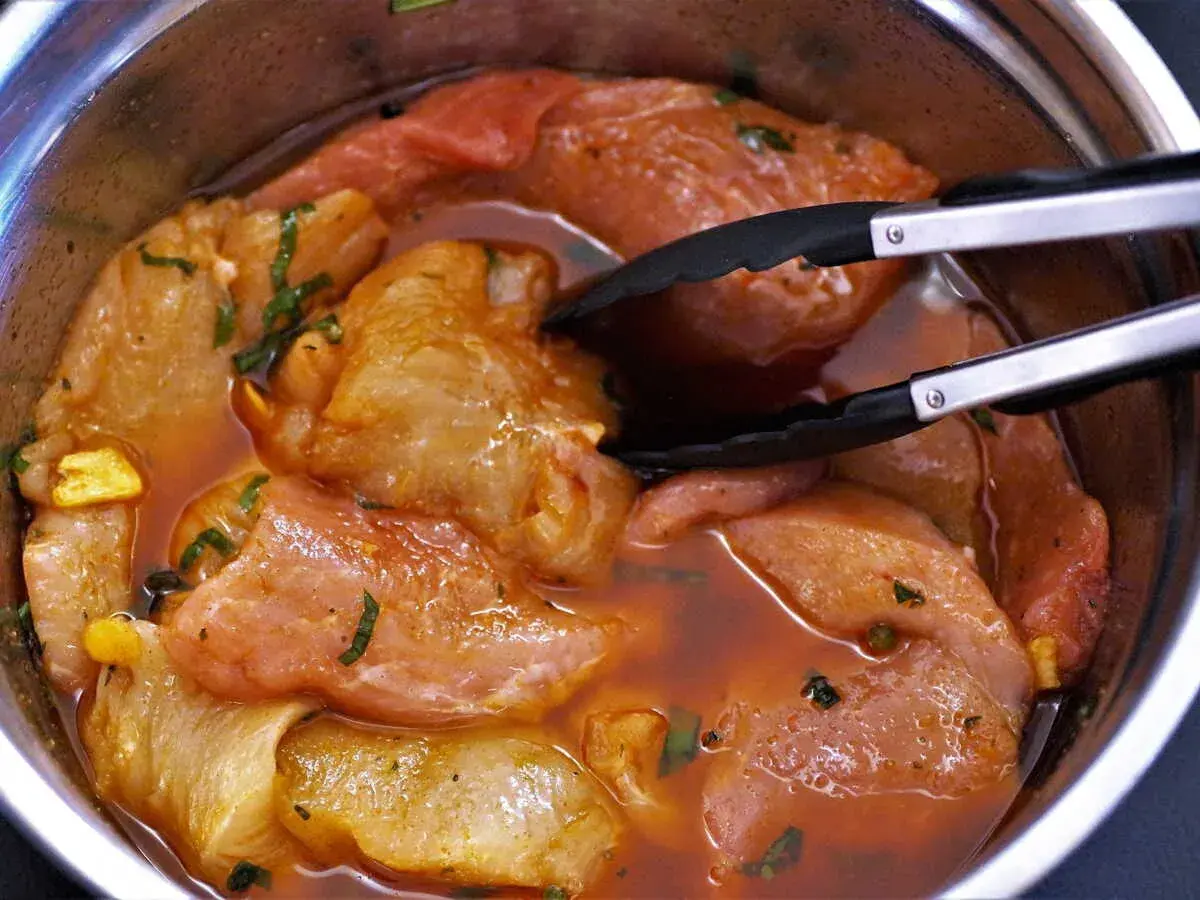 Morceaux de porc marinés dans une sauce rouge, prêts à être cuits. Une araignée de porc se cache dans la marinade.