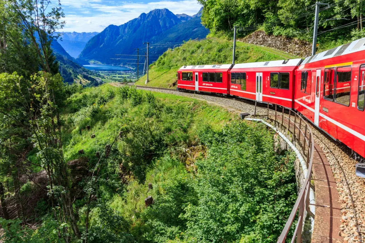 Czerwony pociąg jedzie przez malownicze szwajcarskie góry. Sprawdź swiss travel pass cena, by odkryć te widoki!