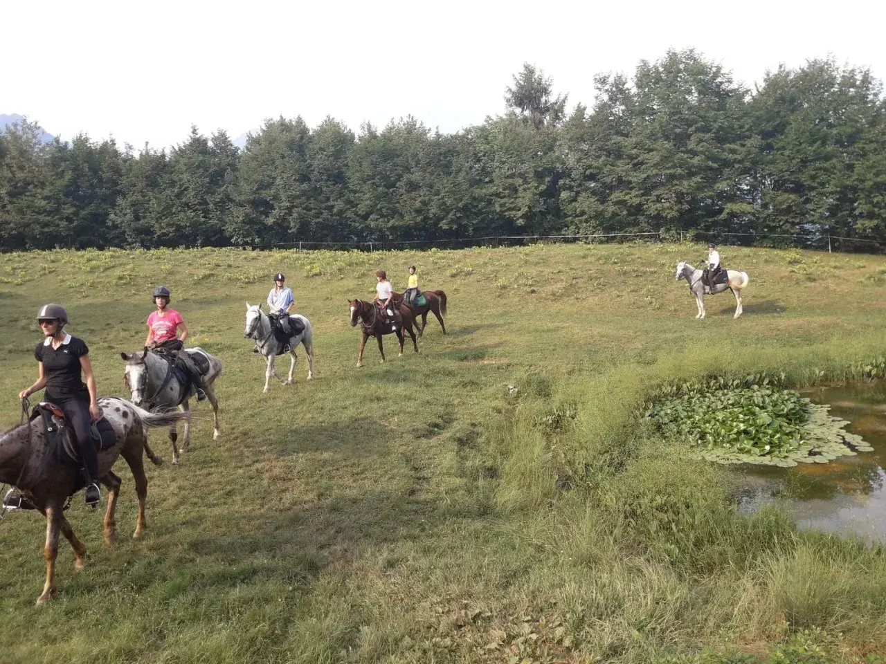 Cavalcata a Toscolano Maderno, un gruppo di persone a cavallo attraversa un prato verde vicino a un laghetto.