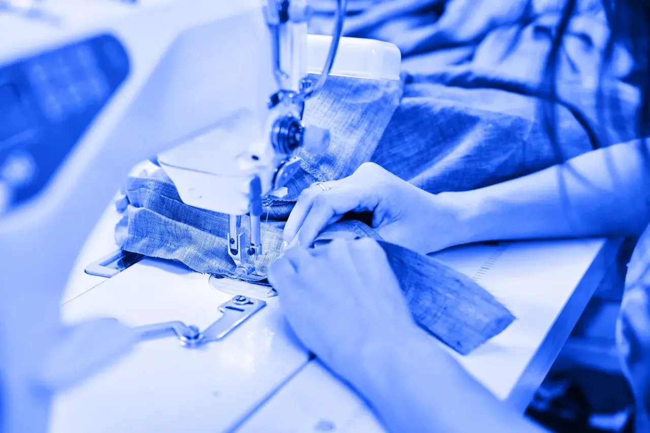 Mains guidant du tissu bleu sous une machine à coudre, un aperçu de l'industrie du vêtement en pleine action.