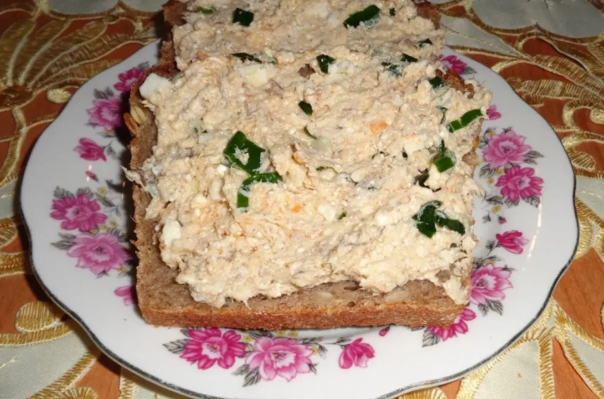 Pyszna pasta z makreli i twarogu z zieloną cebulką na ciemnym chlebie, podana na talerzu z różami.