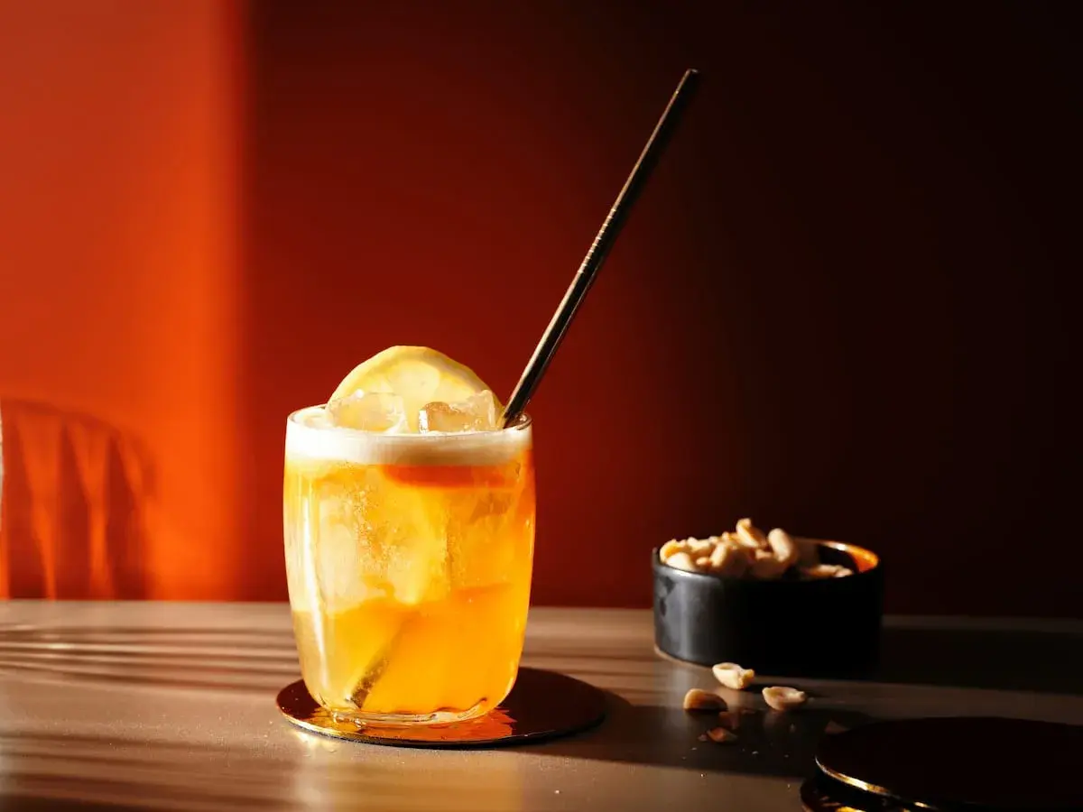 Ein erfrischender Amaretto Sour mit Zitrone und Eiswürfeln, daneben eine Schale Erdnüsse.