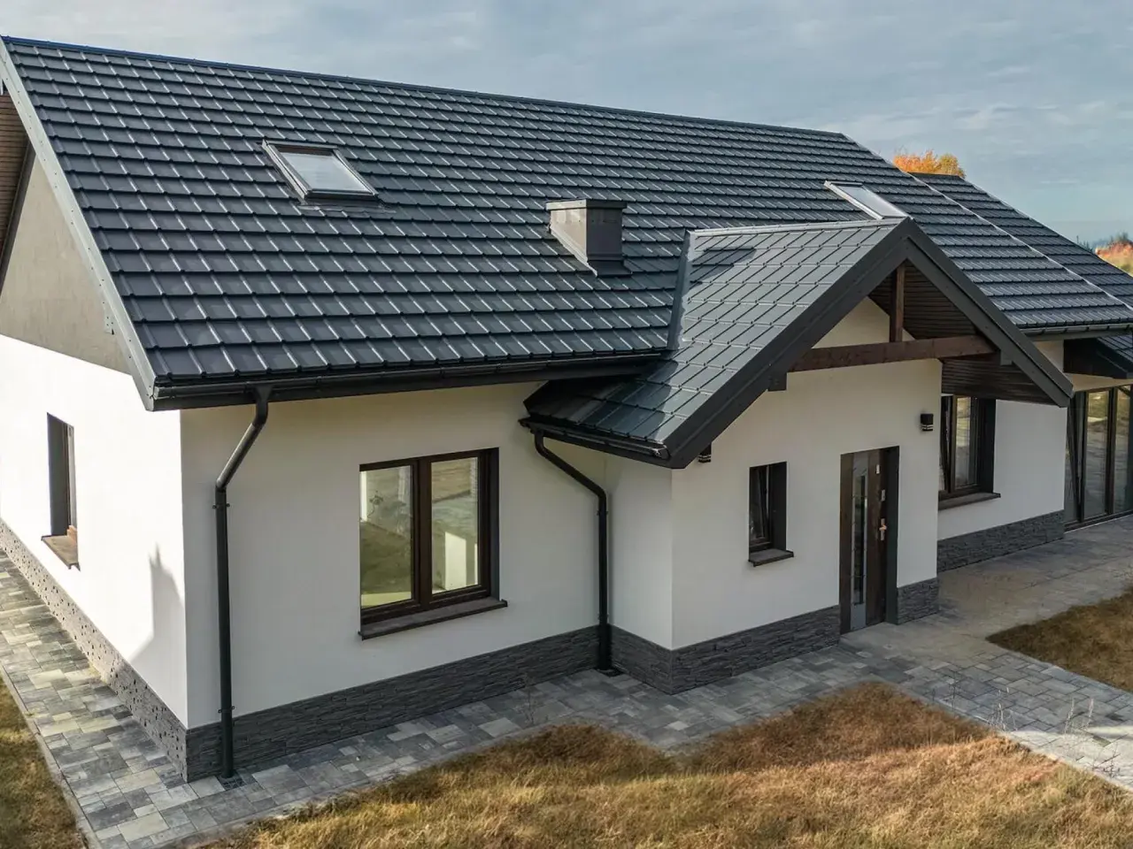 Nowoczesny dom z ciemnym dachem i solidnymi systemami rynnowymi, chroniącymi jego fundamenty.