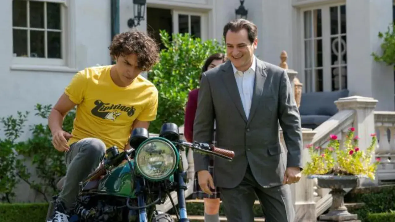 Un ragazzo su una moto e un uomo in giacca e cravatta sorridono. Le recensioni di "Your Honor" potrebbero descrivere questa scena.