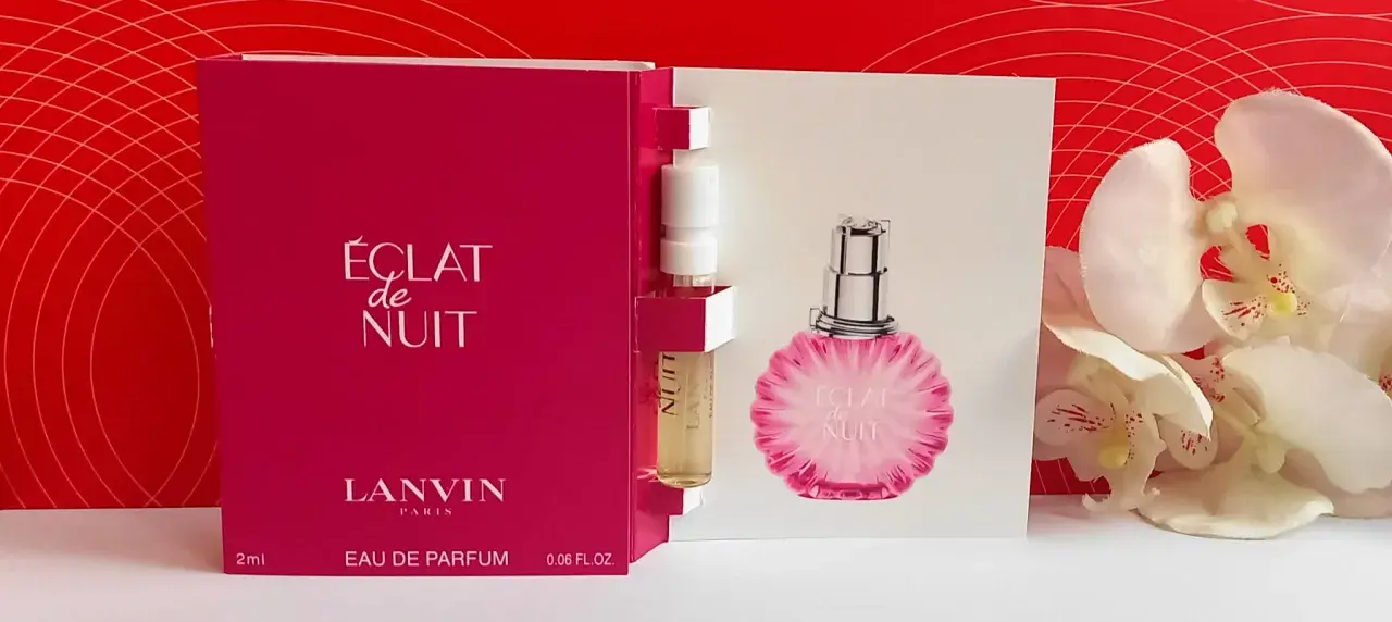 Próbka perfum Lanvin Éclat de Nuit, z buteleczką i kartonikiem z wizerunkiem flakonu, na tle czerwonych wzorów i białych kwiatów.