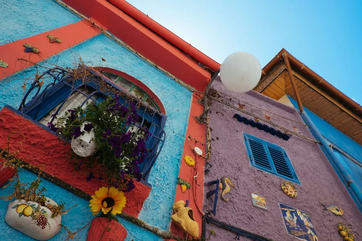 Coloratissimi edifici a Vietri sul Mare: cosa vedere? Finestre fiorite, decorazioni marine e un cielo azzurro.