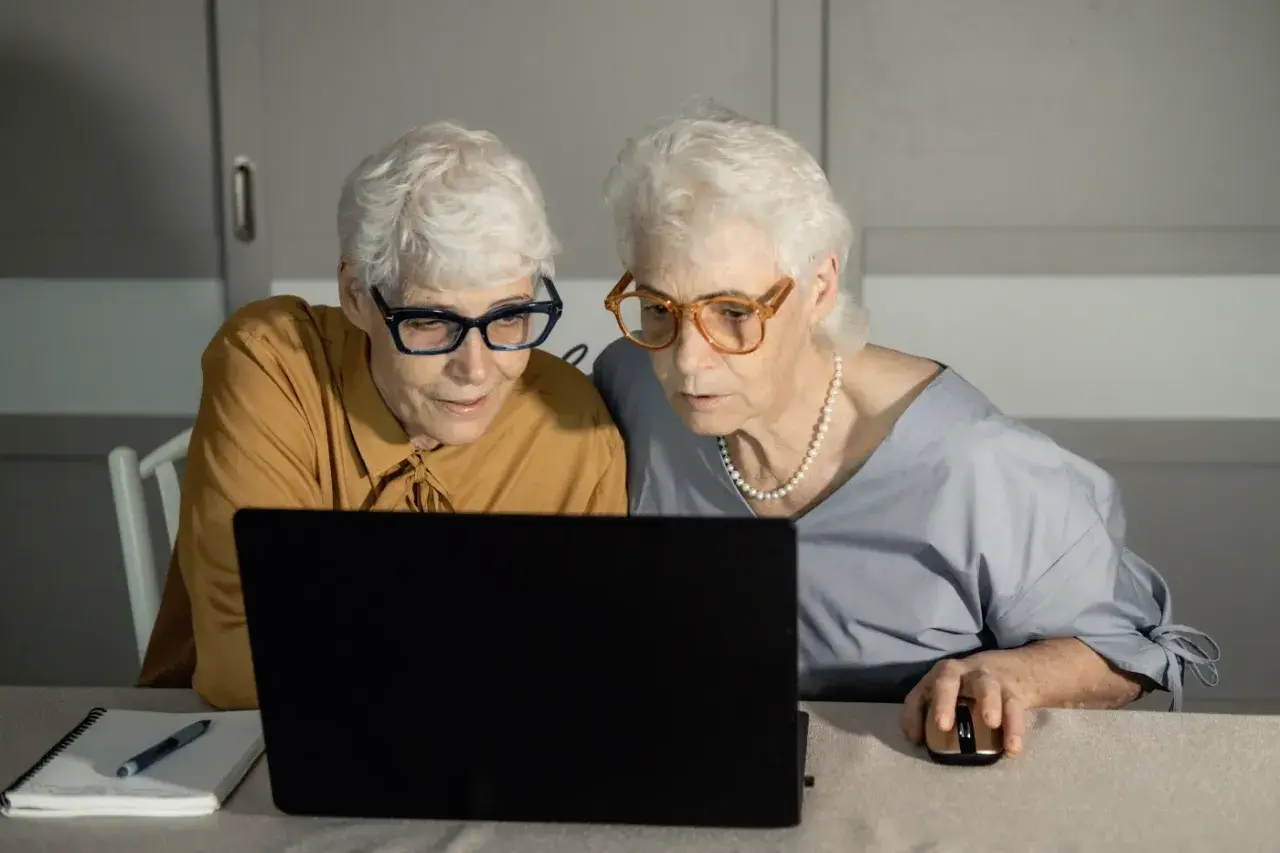 Dwie starsze kobiety w okularach patrzą na ekran laptopa.