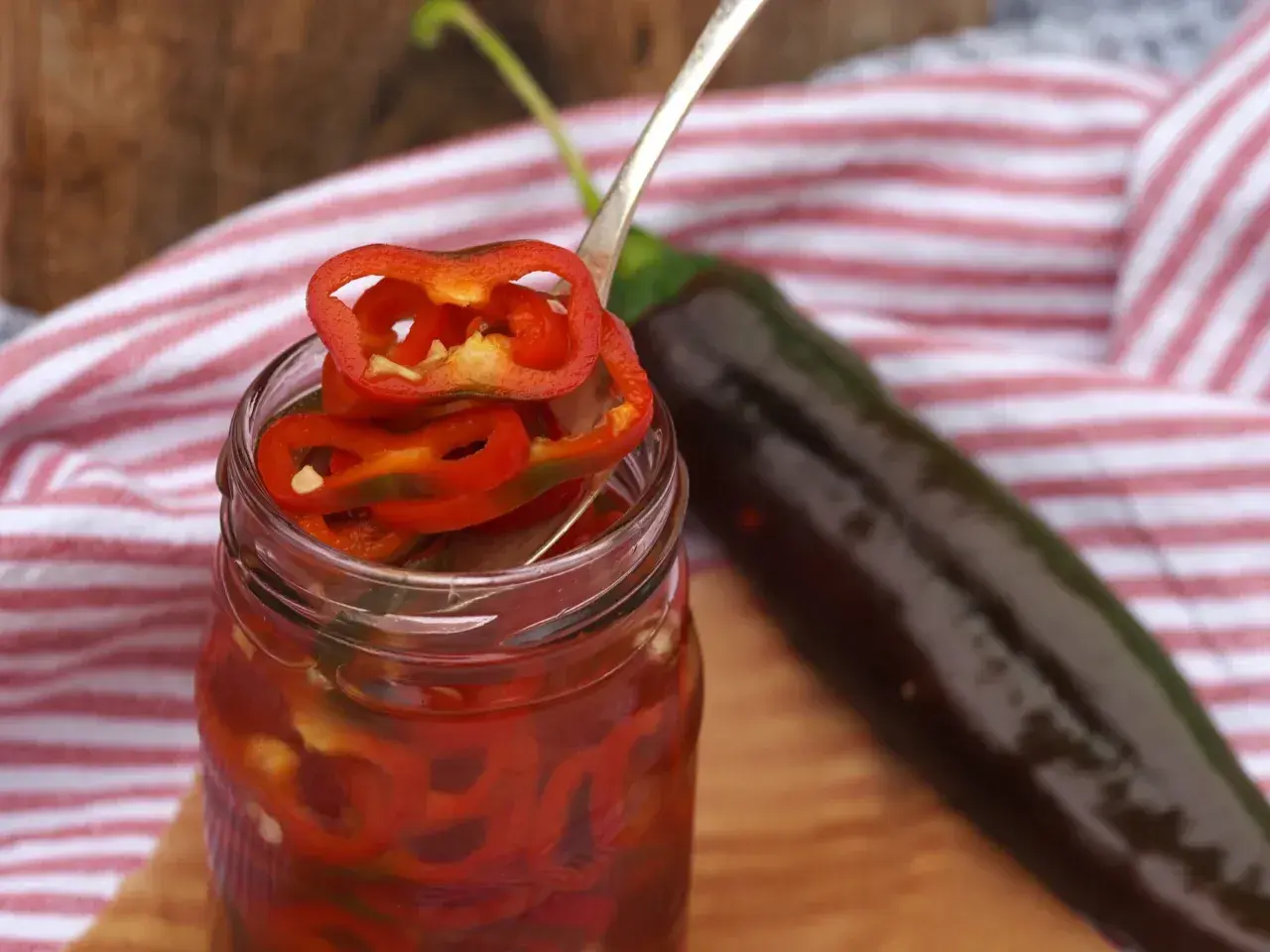 Burk med picklad chili, en sked med chiliringar och en hel mörk chili i bakgrunden.