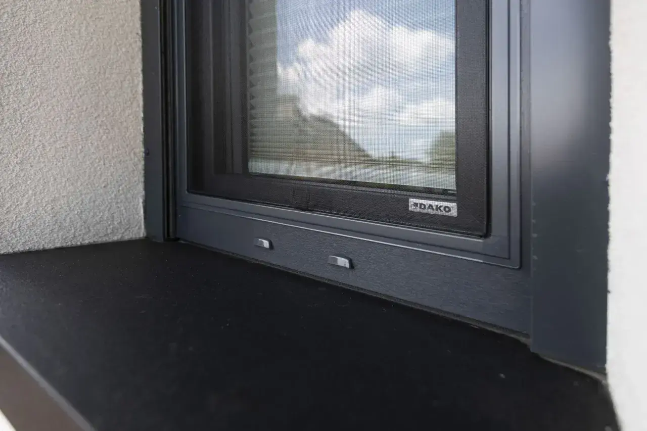 Szary parapet zewnętrzny pod oknem z moskitierą. Zastanawiasz się, czym przykleić parapet zewnętrzny blaszany?