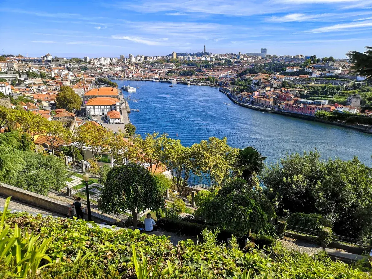 Widok na rzekę Douro i malownicze, kolorowe domy Porto. W oddali widać panoramę miasta, a na pierwszym planie zielony park.