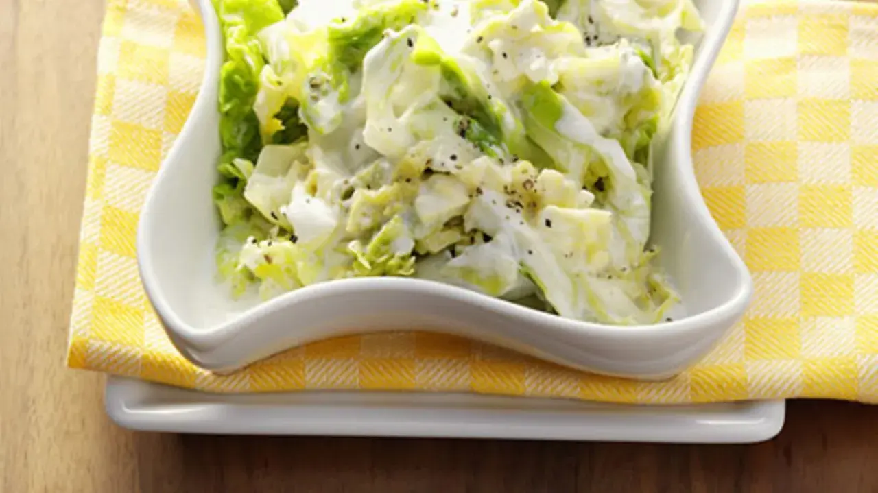 Cremiger Weißkohlsalat, ein einfaches wirsing rezept, serviert in einer weißen Schüssel auf gelb-weiß karierter Serviette.
