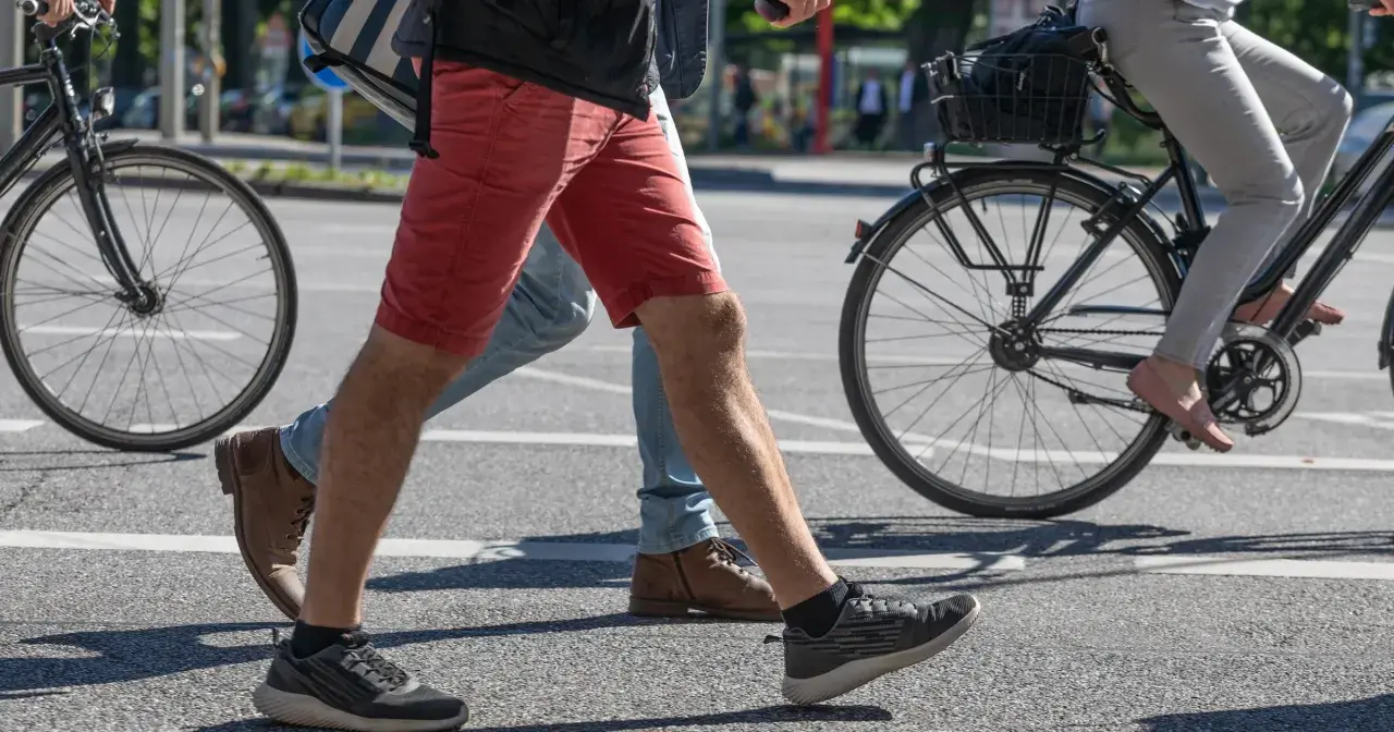 Ludzie przechodzą przez pasy, jeden na rowerze, drugi pieszo. Czy jazda na rowerze odchudza brzuch? To pytanie zadaje sobie wielu.