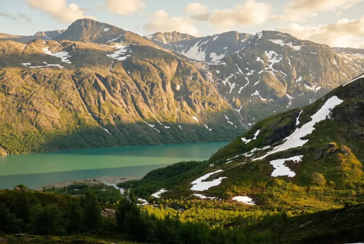 Majestatyczne góry Jotunheimen, jezioro o turkusowej barwie i zielone zbocza z resztkami śniegu.
