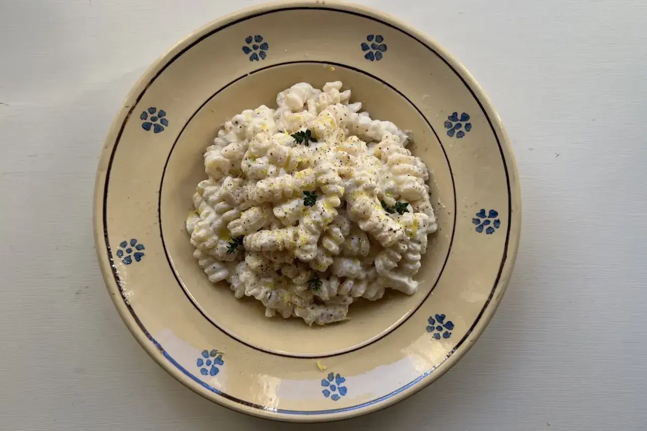 Piatto di pasta ricotta e limone, condita con erbe aromatiche e pepe nero, servita in un piatto di ceramica decorato.