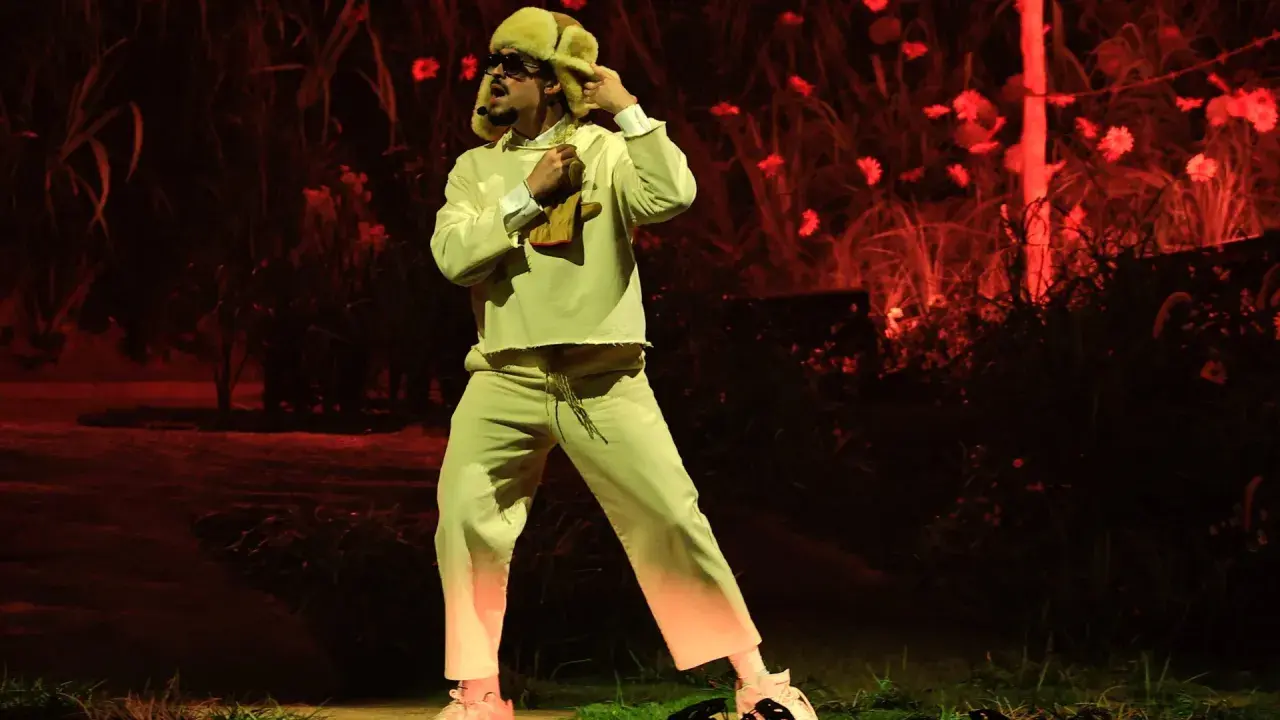 Bad Bunny w beżowym dresie i futrzanej czapce, jakby z "bad bunny café con ron tekst", tańczy na tle czerwonych kwiatów.