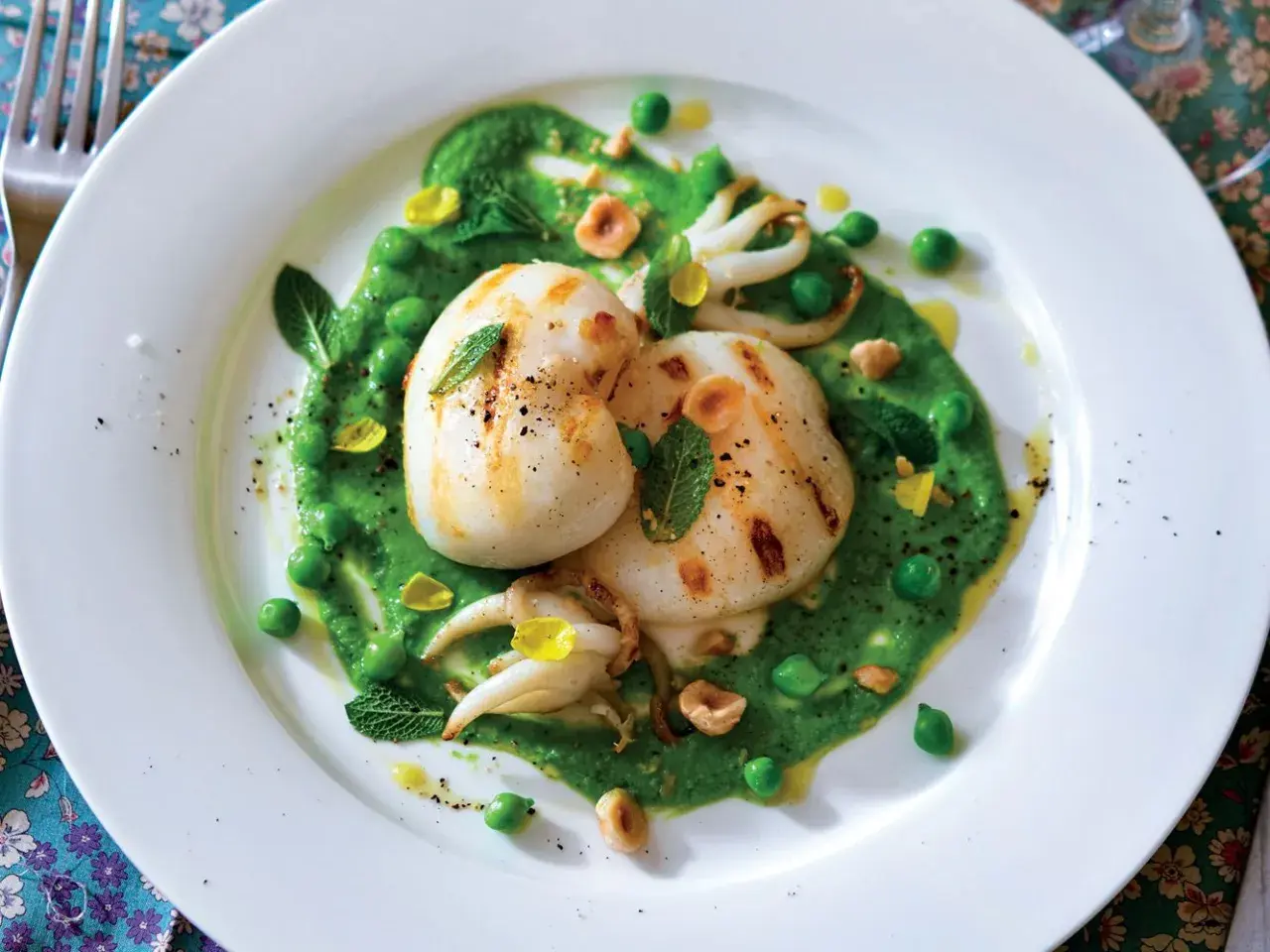 Deliziosi seppie alla griglia su un letto di crema di piselli, guarnite con menta fresca e nocciole tostate.