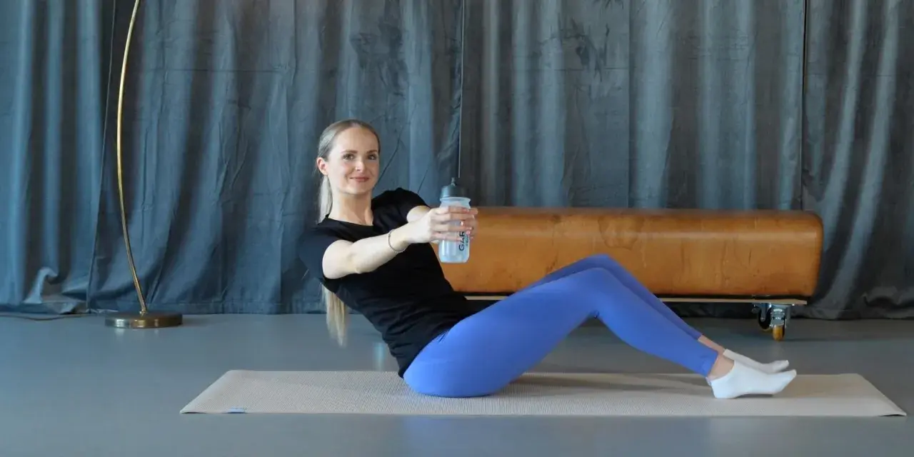 Frau macht isometrisches Training auf einer Matte, hält eine Wasserflasche und dreht den Oberkörper.
