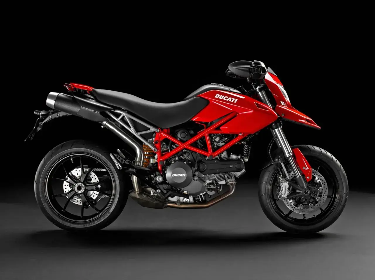 Czerwony Ducati Hypermotard 796 z czarnymi felgami i wydechem, gotowy do jazdy po miejskich ulicach.