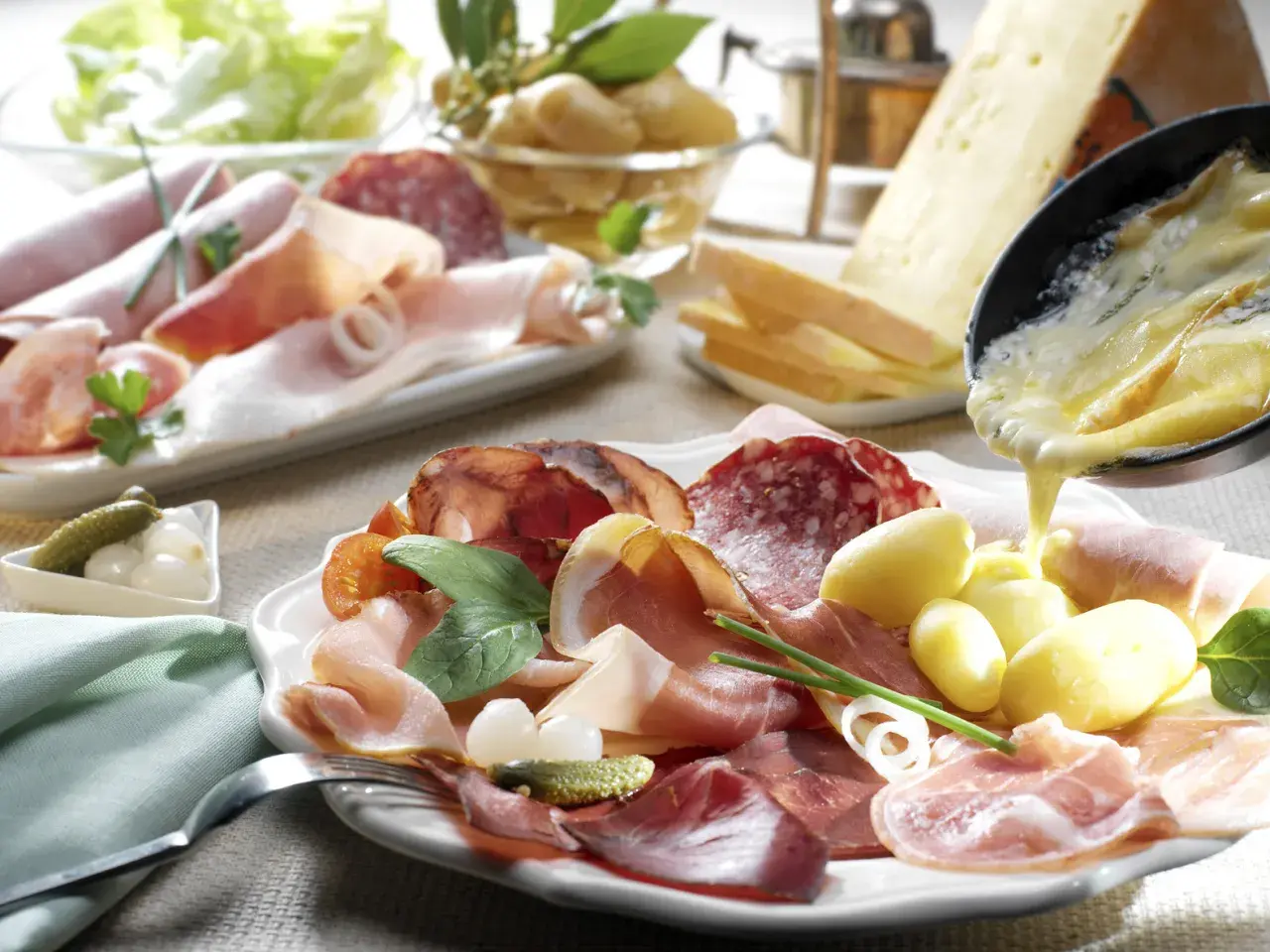 Assiette de charcuterie et pommes de terre, avec du fromage fondu versé dessus. Un délice pour un repas raclette.