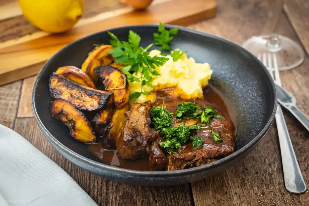 Ein Teller mit Ossobuco, dazu Kartoffelpüree und geröstete Kartoffelspalten. Dieses Ossobuco Rezept original italienisch ist ein Genuss!