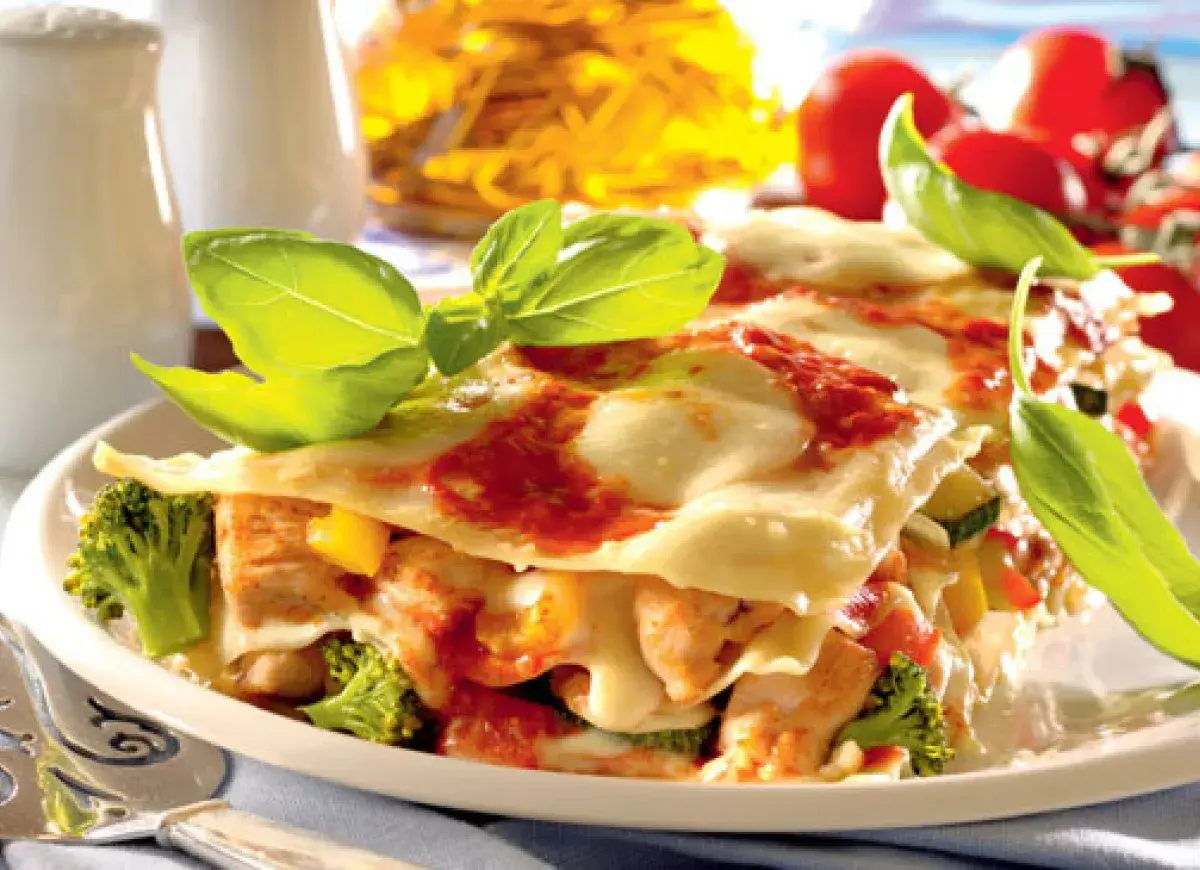 Pyszne lasagne z kurczakiem, brokułami i pomidorami, udekorowane świeżą bazylią.