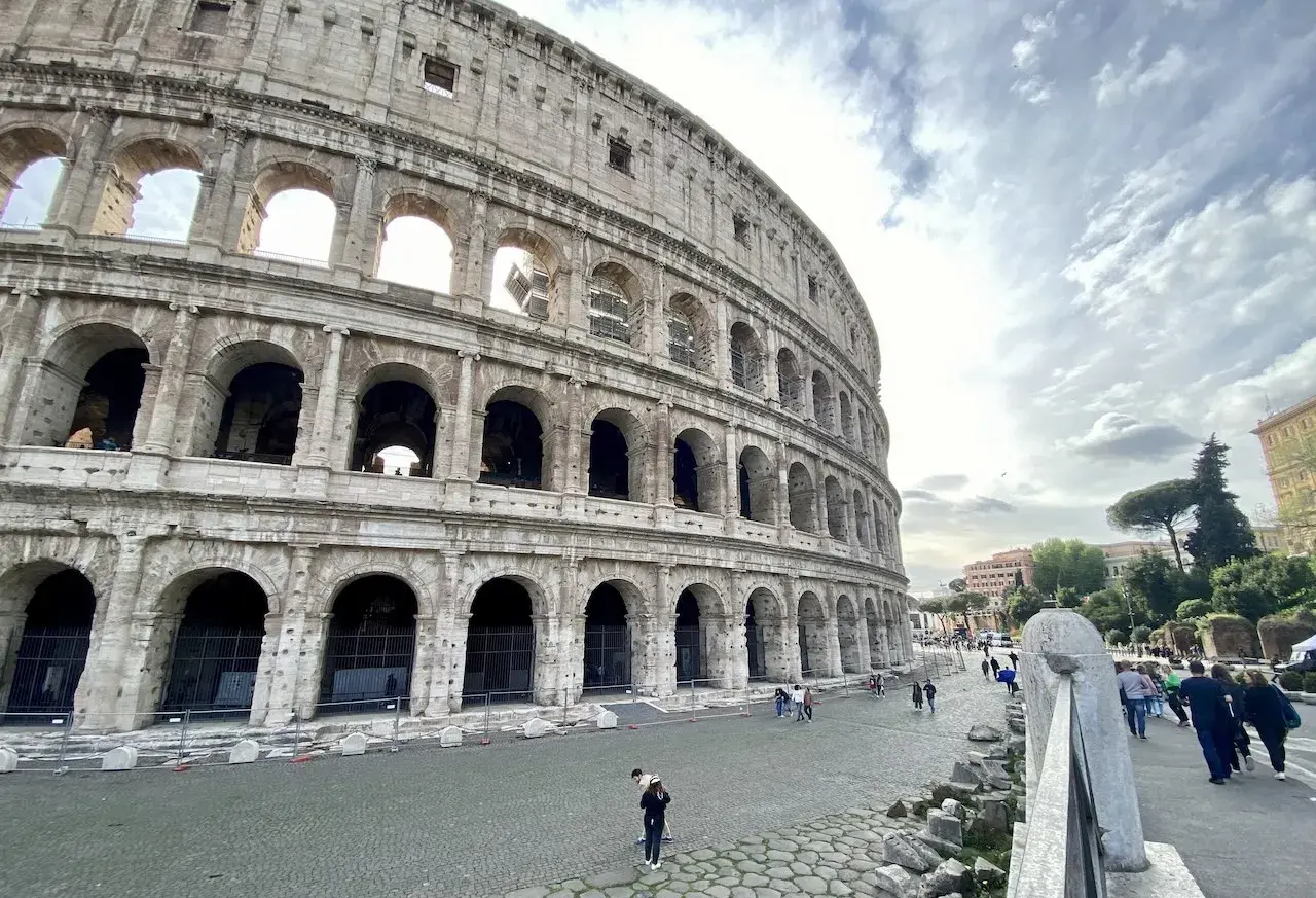 Vue extérieure du Colisée, monument emblématique de Rome. Des touristes profitent de leur visite colisée sous un ciel nuageux.