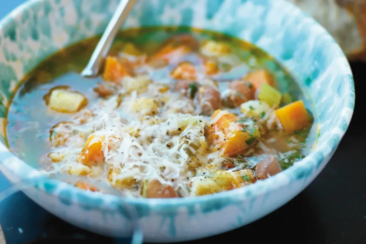 En närbild av en skål med en mustig gryta, kanske ett molokhia recept, med bitar av grönsaker och kött, toppad med riven ost.