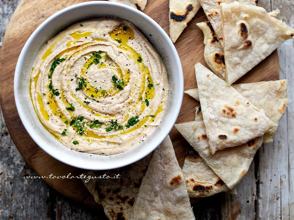 Cremoso hummus di fagioli, condito con olio d'oliva e prezzemolo, servito con pane pita tostato.