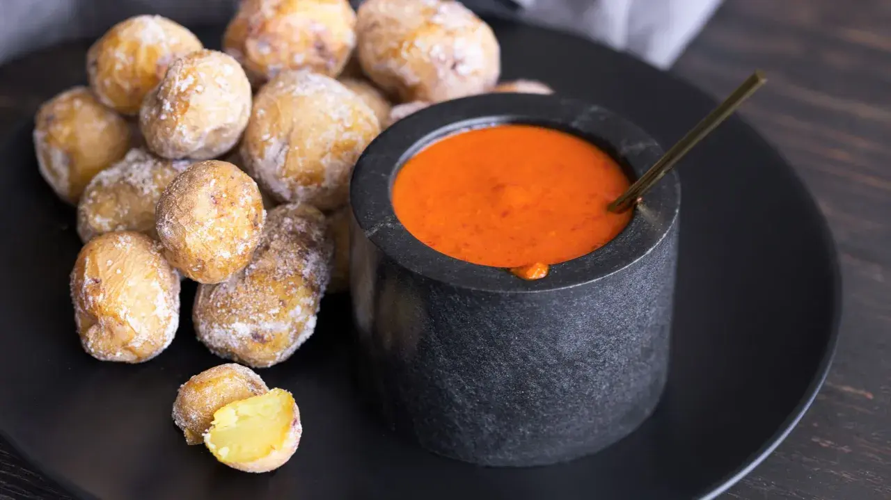 Papas arrugadas cubiertas de sal marina, listas para ser sumergidas en una salsa roja picante.