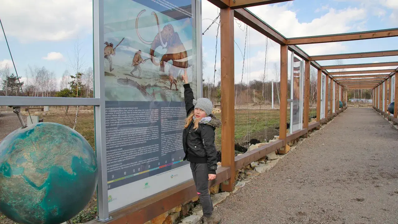 Dziewczynka wskazuje na tablicę informacyjną o prehistorii, jedną z atrakcji Jaworzna. Obok globus.