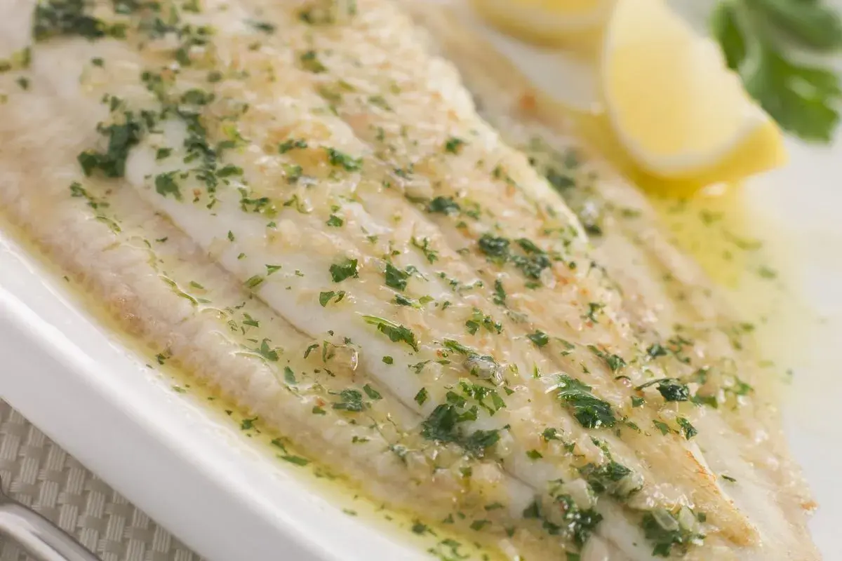 Sogliola alla mugnaia succulenta, cosparsa di prezzemolo fresco e servita con spicchi di limone.