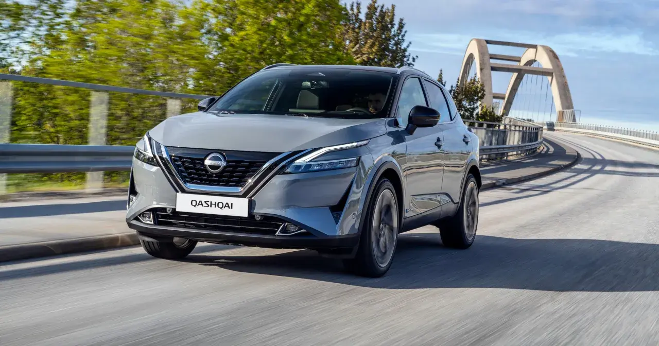 Szary Nissan Qashqai 2024 pędzi po moście z łukowatym wiaduktem w tle.