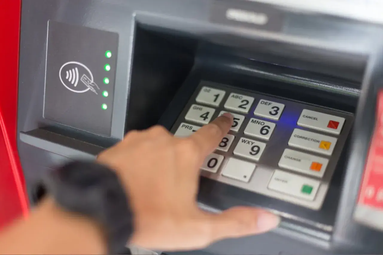 Une main tape un code sur un clavier de distributeur. Comment retrouver son code de carte bancaire ? La sécurité avant tout.