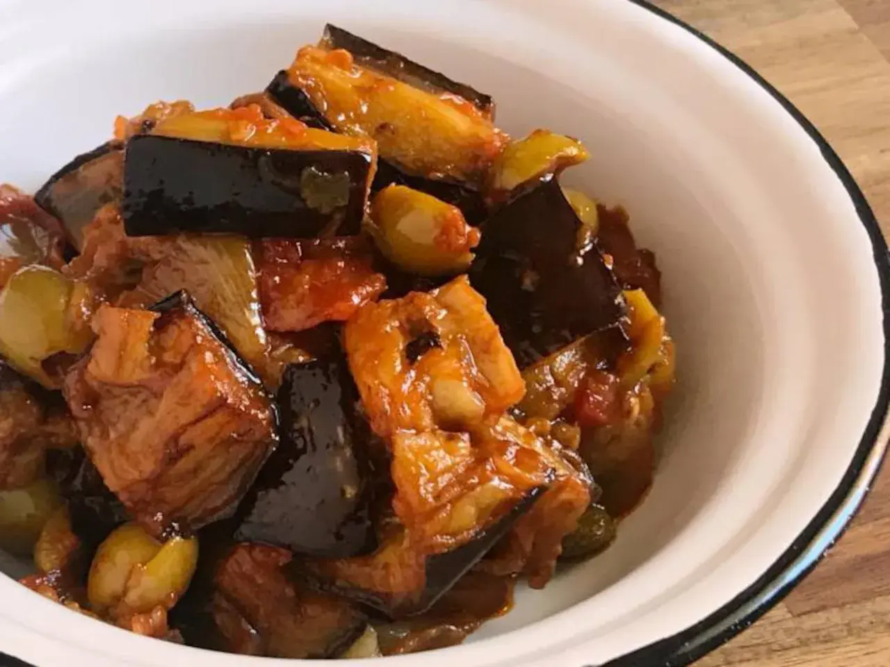 Caponata que es: un delicioso guiso siciliano de berenjenas, aceitunas y tomate, servido en un cuenco blanco.