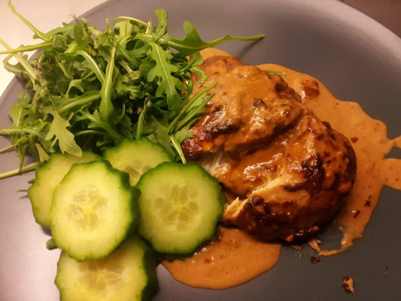 Kyckling i krämig sås med sambal oelek, serverad med ruccola och gurkskivor.