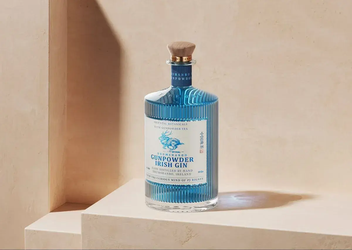 Elegancka butelka Drumshanbo Gunpowder Irish Gin, z niebieskim płynem i wytłoczonym jelonkiem, idealna na prezent dla miłośników ginów.