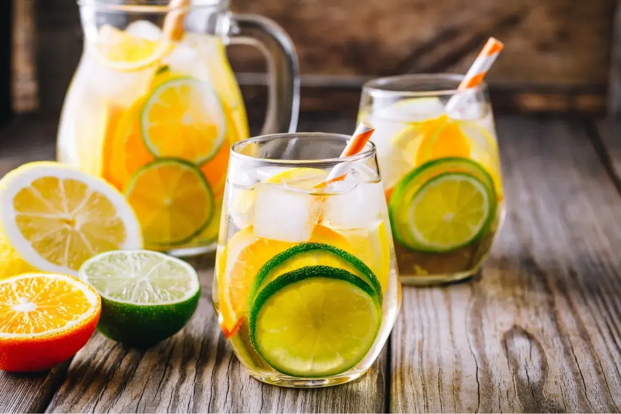Orzeźwiająca biała sangria z plasterkami cytryny, limonki i pomarańczy, podana z lodem w szklankach i dzbanku.