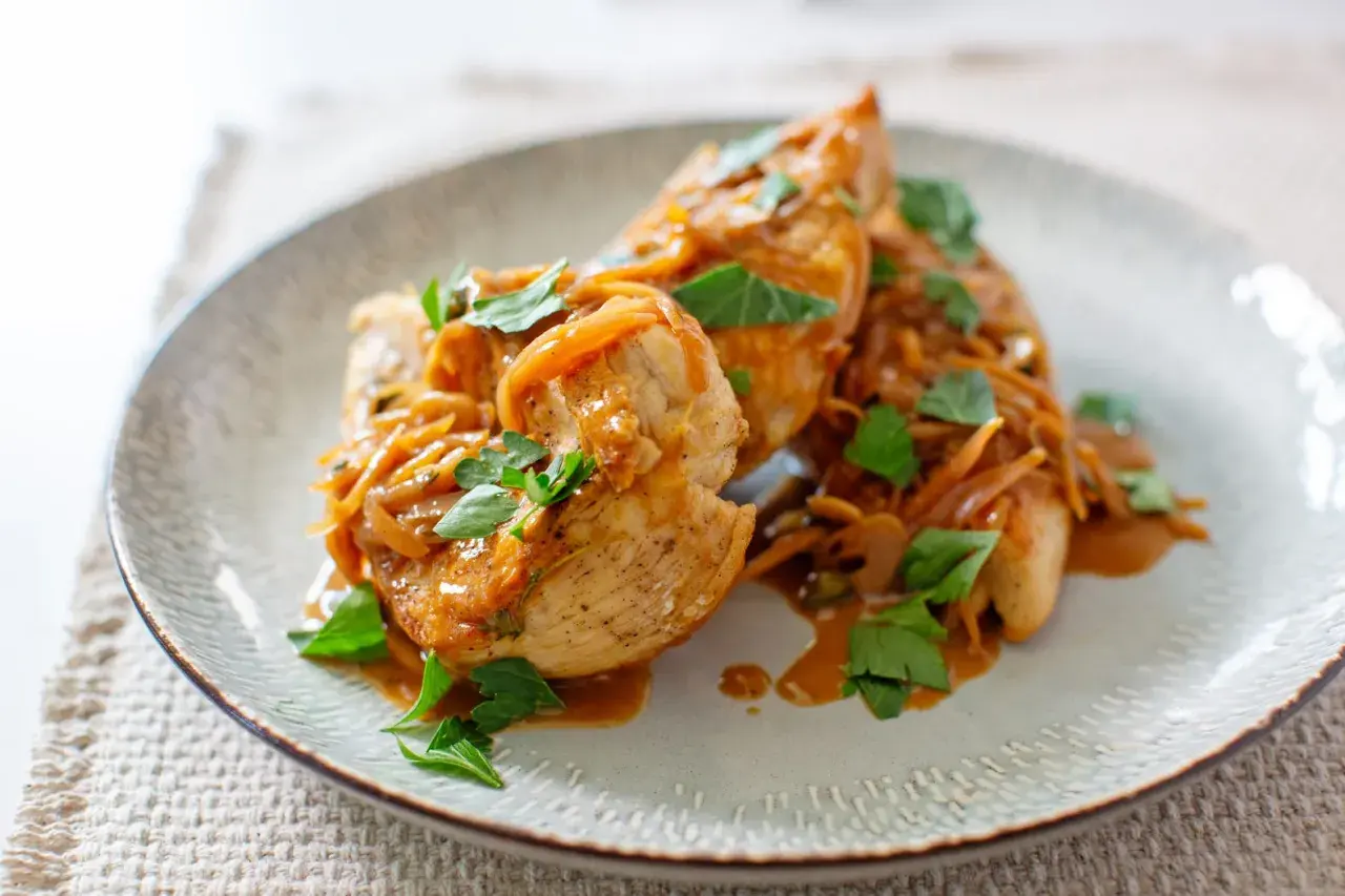 Délicieux sauté de poulet servi sur une assiette, garni d'oignons caramélisés et de persil frais.