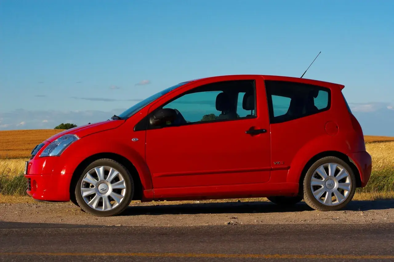 Czerwony Citroen C2 VTR stoi na poboczu drogi, na tle złotego pola i błękitnego nieba.