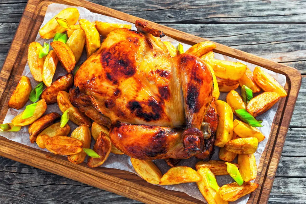 Un poulet rôti doré et croustillant, entouré de pommes de terre rôties et d'oignons verts, prêt à être dégusté.