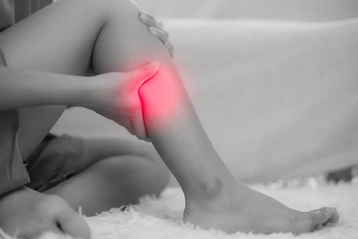 Una persona si tiene la gamba, evidenziata in rosso, per un dolore acuto. Le fitte gambe sono un segnale da non ignorare.