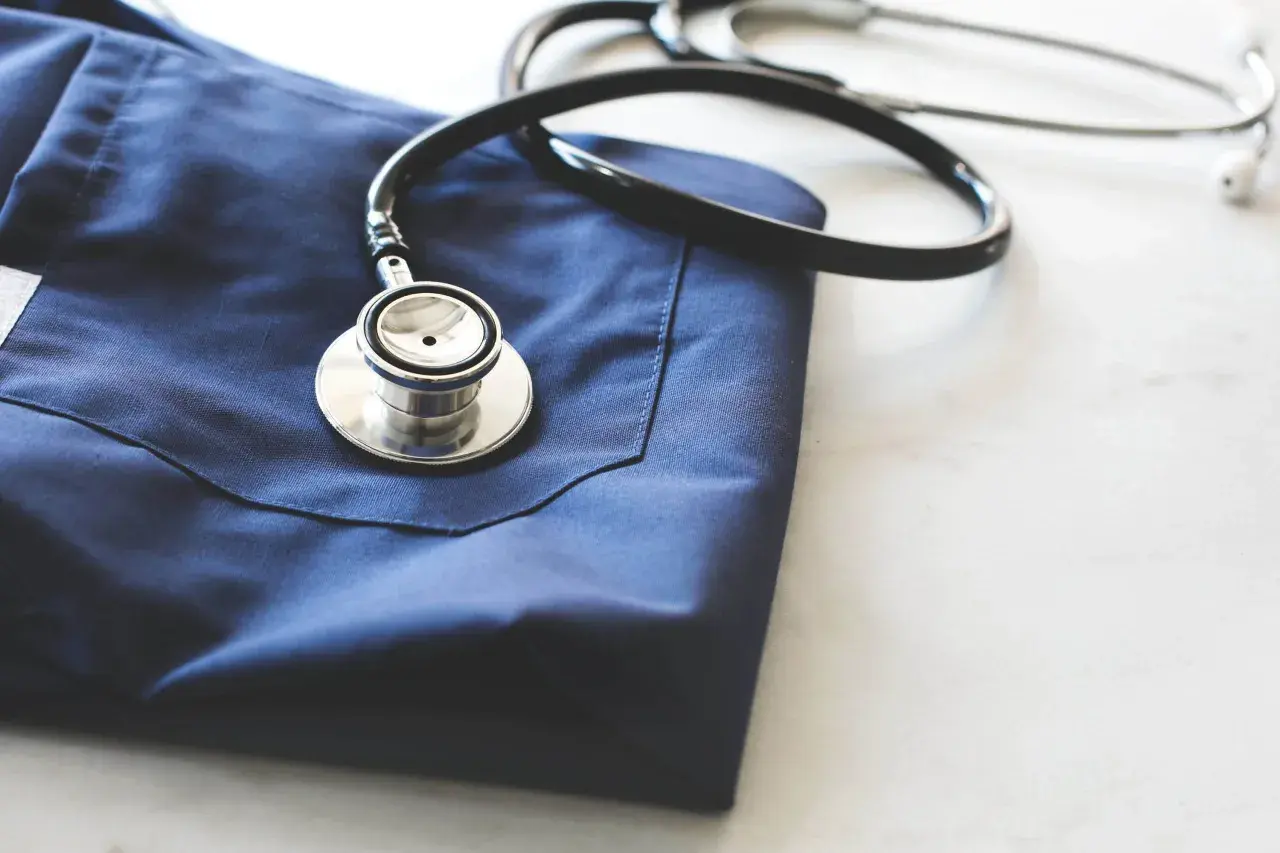 Un camice blu e uno stetoscopio appoggiati su un piano bianco. Immagine evocativa per chi vuole capire come diventare guardia medica.