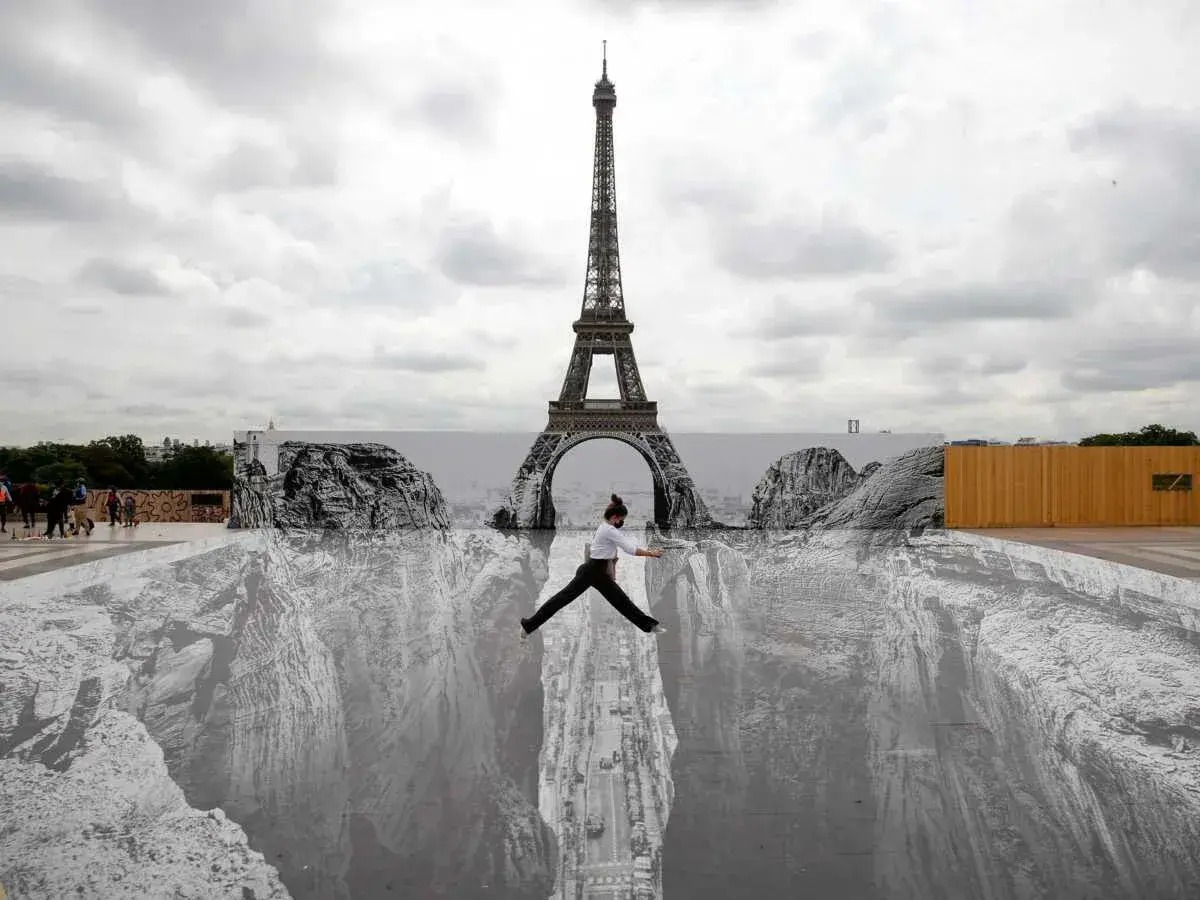 Une femme saute au-dessus d'un gouffre peint au sol, devant la Tour Eiffel. Un **tableau trompe l'oeil** saisissant.