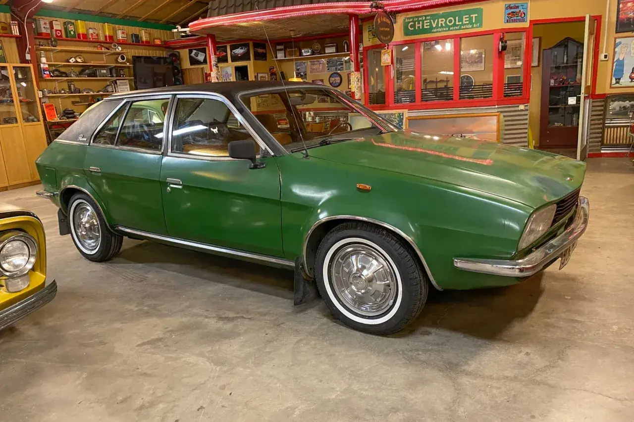 Grön Leyland Princess med svart tak, vit däcksida och kromdetaljer, parkerad i ett garage med retroinredning.