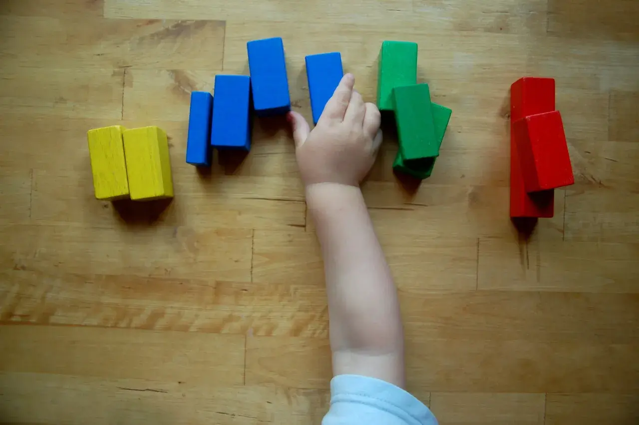 Ein Kinderarm greift nach bunten Holzklötzen. So lernen Kinder spielerisch Farben kennen: Gelb, Blau, Grün und Rot.